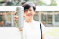 Stylish short hairstyle Asian woman holding, showing reusable insulated stainless steel water bottle, smile,