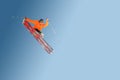 Stylish skier in orange jacket cap and sunglasses in jump does the trick isolated on a blue gradient background