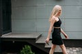 A stylish slender girl with blond long hair and a beautiful smile walks along the city street Royalty Free Stock Photo