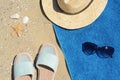 Stylish slippers, straw hat, sunglasses and blue towel on sand, flat lay. Beach accessories Royalty Free Stock Photo