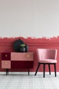 Stylish small pastel pink chair next to trendy pink and burgundy commode