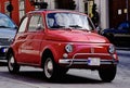 Small Red Italian Made 500 Cc Retro Style Car In Closeup View. Urban Downtown Street Background