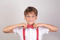 Stylish smiling child in a white shirt with a red bow tie and suspenders and round glasses. The boy holds his hands on the edges Royalty Free Stock Photo