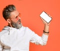 Stylish smiling grey-haired hipster adult man in white hoodie and sunglasses standing looking at smartphone in hand