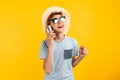 Stylish smiling teen guy in a summer hat, talking on a mobile phone on an yellow background