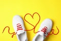 Stylish sneakers and red shoe laces in shape of heart on yellow background, flat lay Royalty Free Stock Photo