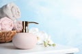 Stylish soap dispenser, towels in wicker basket and flowers on table Royalty Free Stock Photo