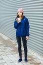 Stylish sporty brunette woman in trendy urban outwear posing with big white disposable cup straw cold rainy fall day against strip