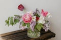 Stylish spring bouquet on rustic wooden bench. Beautiful lilacs, tulips and daffodils in glass vase on background of grey wall. Royalty Free Stock Photo