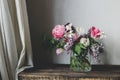 Stylish spring bouquet on rustic wooden bench. Beautiful lilacs, tulips and daffodils in glass vase on background of grey wall and Royalty Free Stock Photo