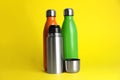 Stylish stainless thermo bottles on yellow background