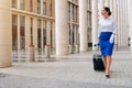 Stylish stewardess in uniform in white formal gloves sets off for work with a suitcase. Mysterious girl in a business suit looks Royalty Free Stock Photo