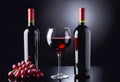 A stylish still life featuring wine glasses filled with red wine, a bottle of red wine, and a bunch of fresh red grapes on a black Royalty Free Stock Photo