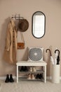 Stylish storage bench with different pairs of shoes near beige wall in hall