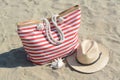 Stylish striped bag with straw hat and seashell on sandy beach Royalty Free Stock Photo