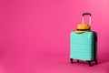 Stylish suitcase with hat on color background