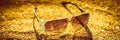 Stylish sunglasses lie on a sand, golden tone