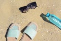 Stylish sunglasses, slippers and bottle of water on sand. Beach accessories