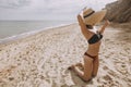 Stylish tan girl in hat sitting on beach. Fashionable young woman covering with straw hat, relaxing on sandy beach near sea. Royalty Free Stock Photo