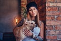 A stylish tattoed blonde female in t-shirt and jeans holds a cute dog. Royalty Free Stock Photo