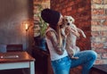 A stylish tattoed blonde female in t-shirt and jeans holds a cute dog. Royalty Free Stock Photo