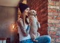 A stylish tattoed blonde female in t-shirt and jeans holds a cute dog. Royalty Free Stock Photo