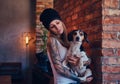 A stylish tattoed blonde female in t-shirt and jeans holds a cute dog. Royalty Free Stock Photo