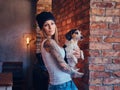 A stylish tattoed blonde female in t-shirt and jeans holds a cute dog. Royalty Free Stock Photo