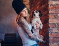 A stylish tattoed blonde female in t-shirt and jeans holds a cute dog. Royalty Free Stock Photo