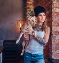 A stylish tattoed blonde female in t-shirt and jeans holds a cute dog. Royalty Free Stock Photo