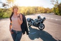 Stylish tattoed girl with a leather jacket poses against the background of a motorcycle by the road. Motorcycle local Royalty Free Stock Photo