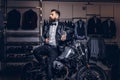 Stylish tattooed bearded man with dressed in black leather jacket and bow tie posing near retro sports motorbike at men