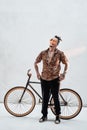 Stylish tattooed gangster freak in hawaiian shirt and sports pants standing next to a custom made bicycle, looks at the