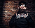 A stylish tattooed guy in a black hoodie and sunglasses. Studio photo against brick wall