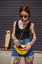 stylish tattooed woman listening music in earphones and putting smartphone in waist