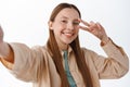 Stylish teenage girl, female student posing with v-sign for selfie, holding smartphone, taking picture on mobile phone Royalty Free Stock Photo