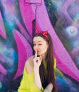 A stylish teenage girl in a yellow jacket and blue jeans poses near a graffiti wall Royalty Free Stock Photo