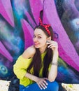 A stylish teenage girl in a yellow jacket and blue jeans poses near a graffiti wall Royalty Free Stock Photo