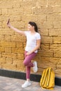 Stylish teenager girl takes a selfie in city over stone wall background. Royalty Free Stock Photo