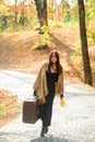 Stylish traveler, autumn woman. Full length of a sensual woman wearing a sweater walking with a travel bag over autumnal