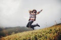 Stylish traveler girl in hat with backpack jumping in mountains.