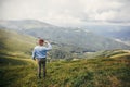 Stylish traveler man in hat standing on top of sunny mountains i