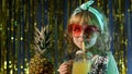 Stylish trendy child kid girl at disco party cyberpunk club with pineapple fruit drinking juice