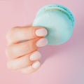 Stylish trendy female manicure on pink background. Girl holds hands blue macaron cookies through hole