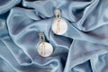 Stylish trendy golden earrings on crumpled blue fabric bacground. Fashionable women& x27;s jewelry with shell rock