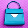 Stylish turquoise leather women\'s flap bag with top handle and silver accent and hardware on a fun pink background