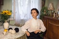 A stylish Ukrainian woman in vintage clothes sits at a table in a cozy apartment with retro furniture