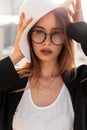 Stylish urban portrait of a young beautiful girl with glasses in a fashionable black blazer and a white T-shirt with a hat in the Royalty Free Stock Photo