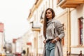 Stylish urban young woman in a fashionable knitted sweater in a elegance trench coat in a blue jeans posing in the street.