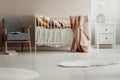 Stylish vintage armchair next to white wooden crib with pastel pink blanket, pillows and cotton ball lights